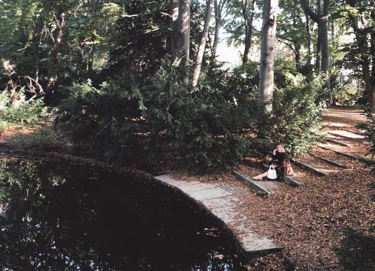 Woman in the woods wearing secondhand skirt and blazer with gold necklaces